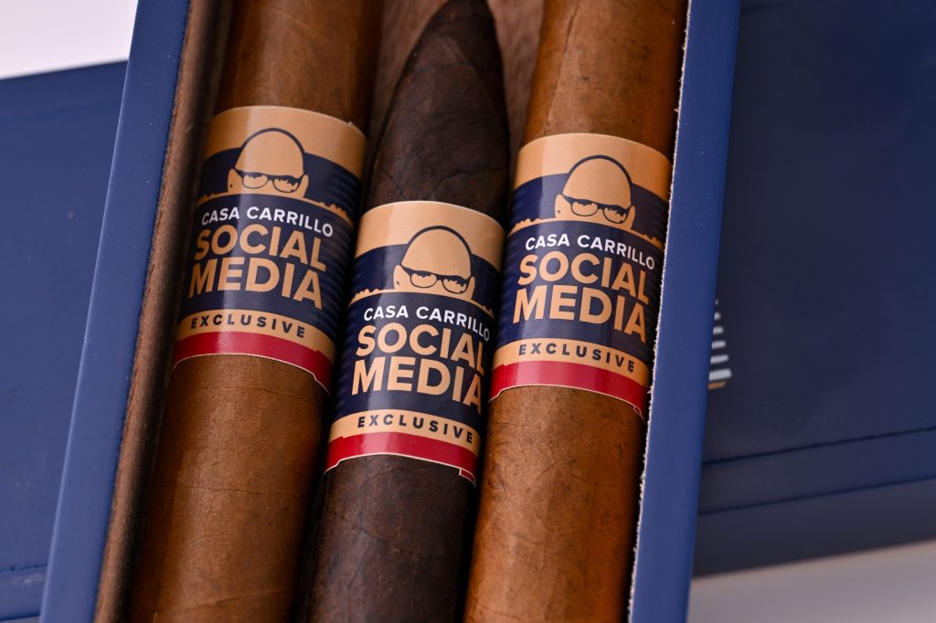 Close-up of Casa Carrillo Social Media Exclusive cigars inside a blue box, showing brown wrappers and navy, tan, and red cigar bands.